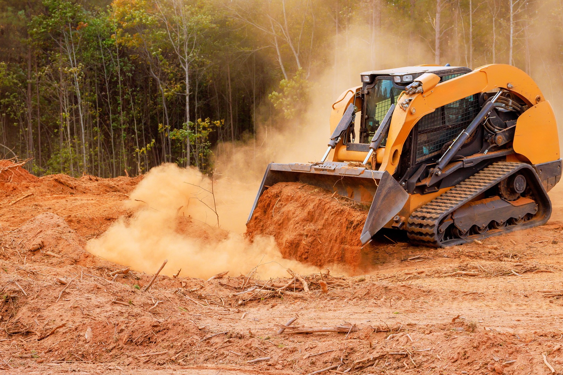 Excavator moves dirt in forested area while creating space for construction work during daylight